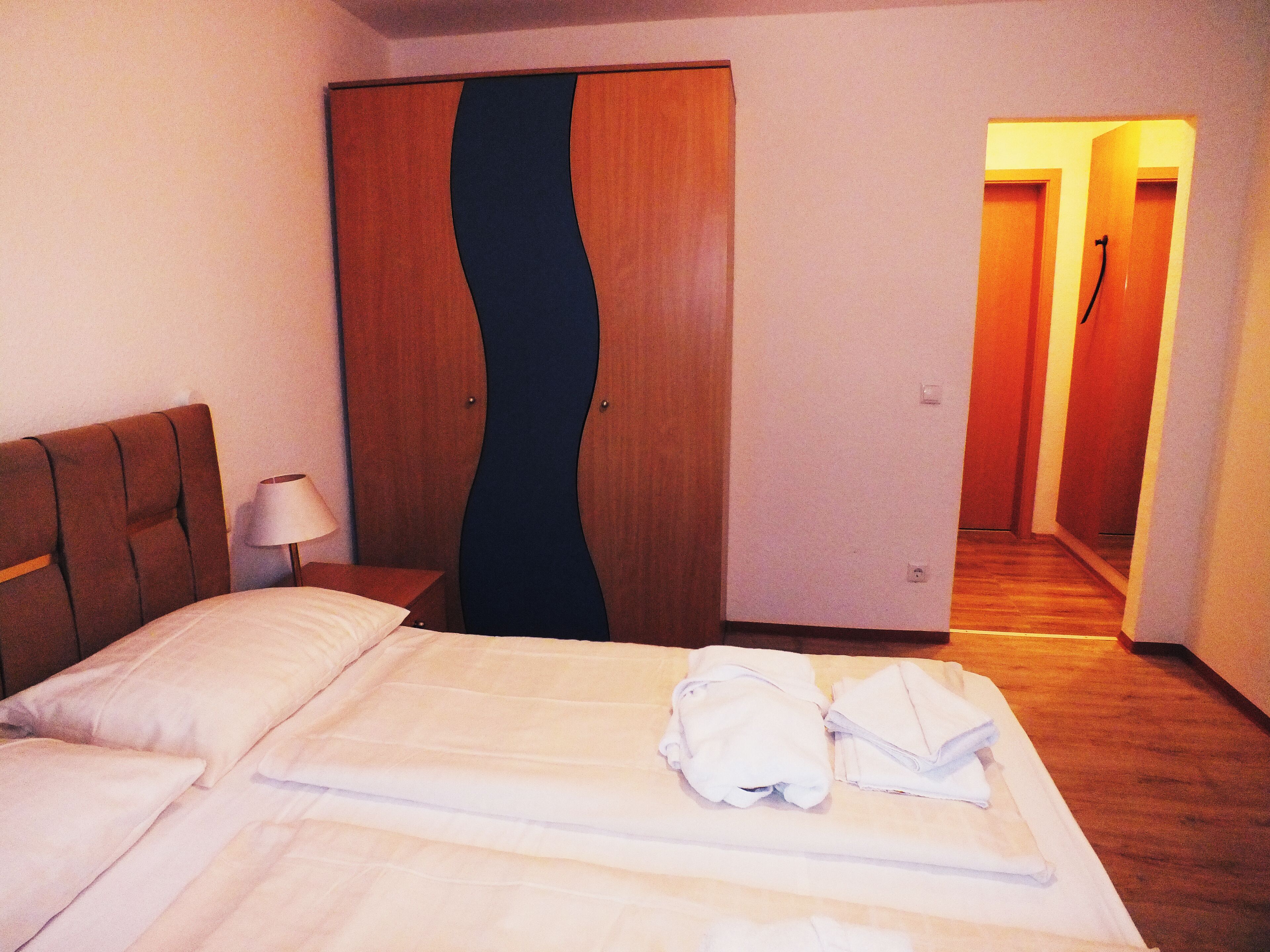 Une chambre d’hôtel comprenant un lit, une table de chevet, une lampe, une armoire et un couloir.