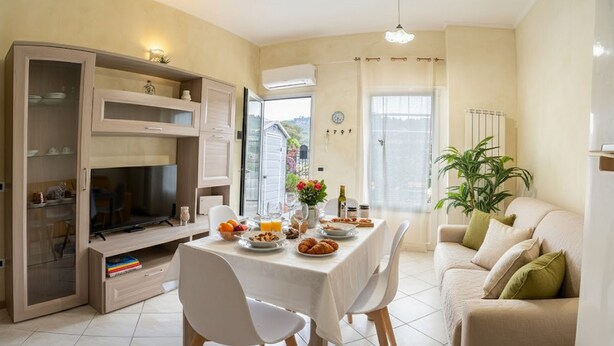 A dining area with a table set for breakfast, a television, and a sofa. - Littardi Smart Suite (Imperia)