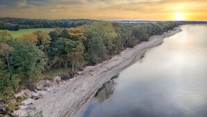 A coastal landscape with a sandy beach, dense trees, and a calm body of water.