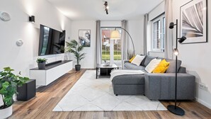 A modern living room with a grey sectional sofa, a flat-screen TV, a coffee table, and a floor lamp.