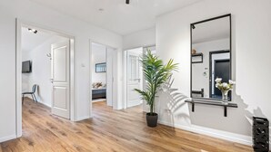 A modern interior with a wooden floor, white walls, a large mirror, and a potted plant.