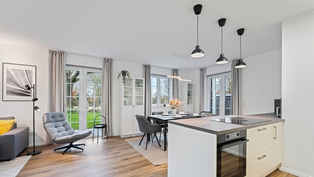 A modern kitchen with a central island, built-in oven, and pendant lights.