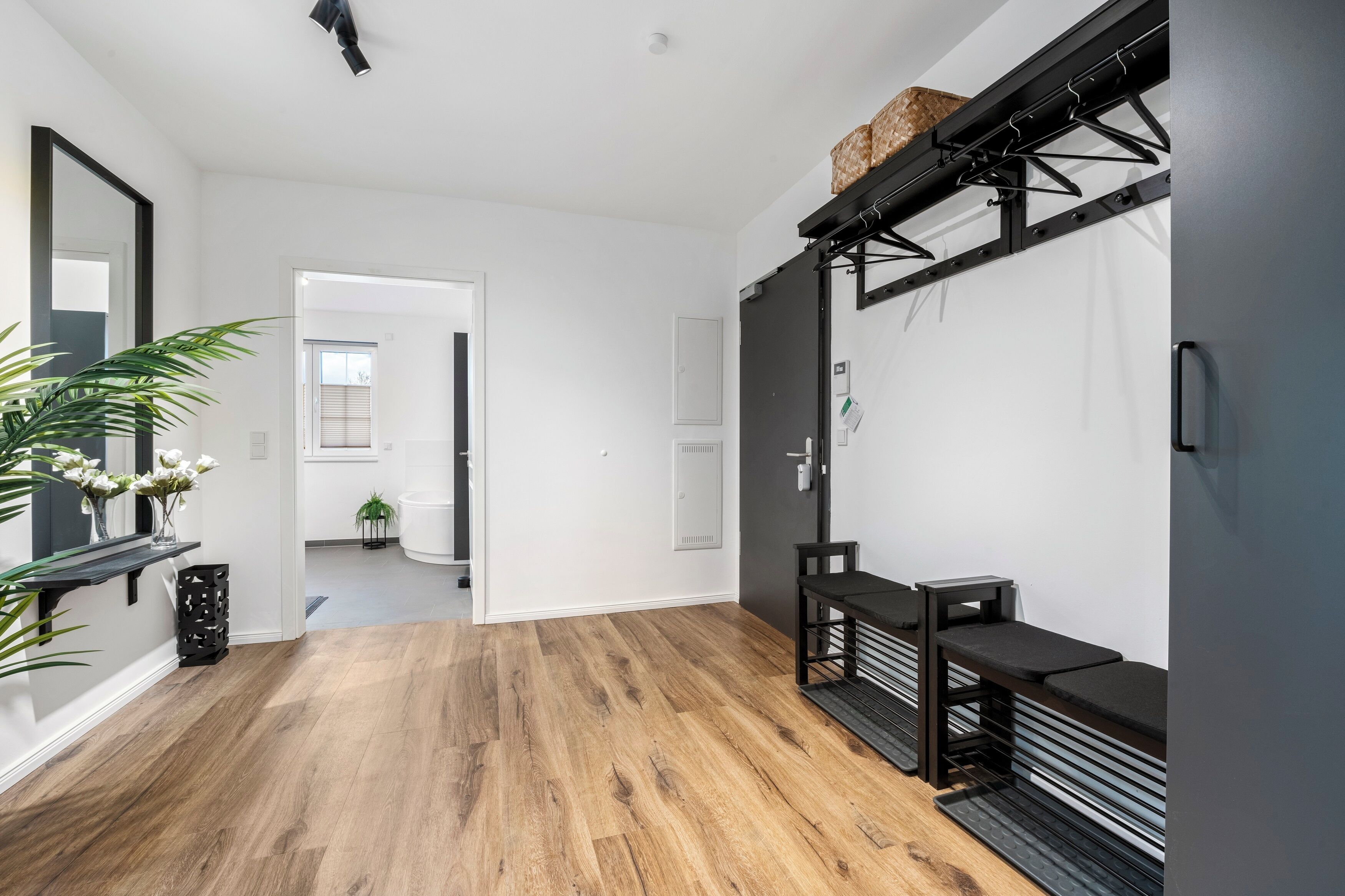A modern interior with a wooden floor, a bench, a mirror, and a wall-mounted rack.