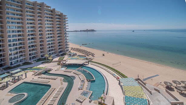 Ein Resort mit einem großen Gebäude, einem Poolbereich und einem Strand.