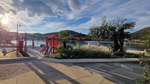 A park with a playground, a small pavilion, and a body of water in the background.