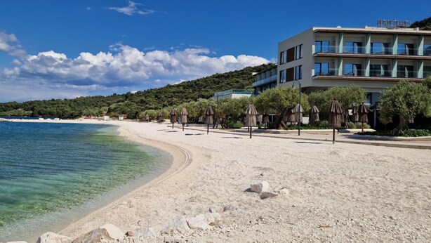 A beach with clear water, a sandy shore, and a building with balconies.