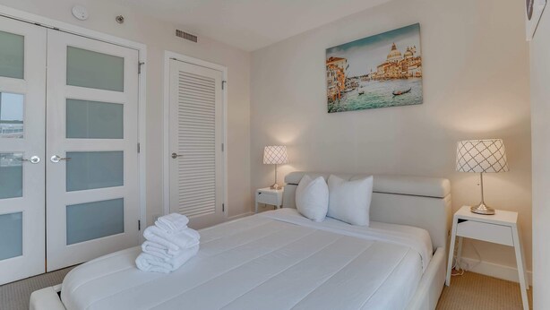 Une chambre d’hôtel avec un lit, des rideaux blancs, un tableau représentant Venise et deux lampes de chevet.