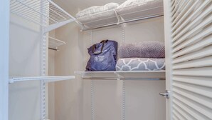 Un placard avec des étagères blanches, un sac violet et du linge de lit à motifs.