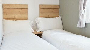 A room with two beds, each with a wooden headboard, white bedding, and a nightstand.