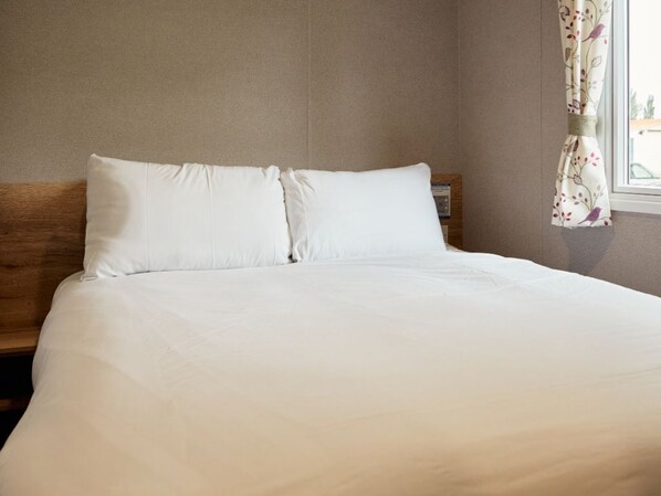 Una cama bien hecha con ropa blanca en una habitación con cabecera de madera y una ventana con cortinas florales.
