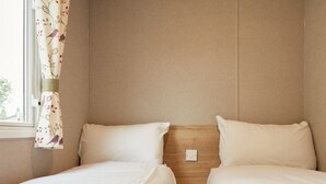 A hotel room with two single beds, a wooden headboard, and a window with floral curtains.