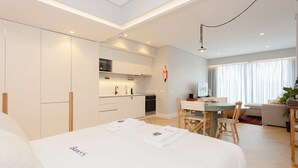 Et moderne hotelværelse med en stor seng, et spiseområde med bord og stole, et tekøkken og en opholdsstue med en sofa og en plante.
