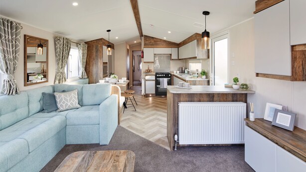 A modern living room with a sectional sofa, a wooden coffee table, and a kitchen area with a stove and cabinets.