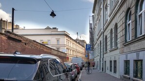 Une rue bordée de voitures garées et où l’on aperçoit un vélo. Des immeubles s’alignent le long de la rue, et des panneaux indiquent les zones de stationnement ainsi qu’un panneau de signalisation « stop ».
