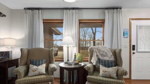 Una habitación con dos sillones a cuadros, una mesita redonda con una lámpara y vistas al exterior a través de amplios ventanales.