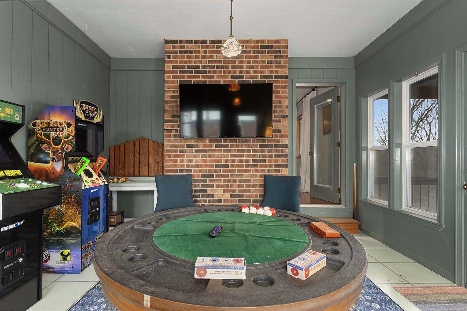 A room with a brick fireplace, a mounted TV, a pool table, and arcade games.