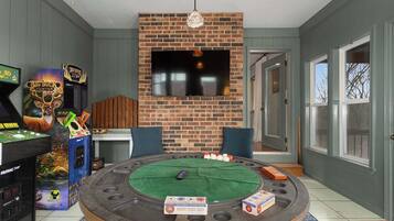 A room with a brick fireplace, a mounted TV, a pool table, and arcade games.