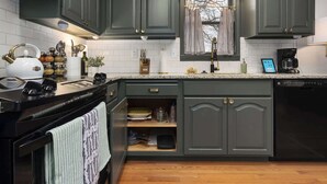 Una cocina con armarios oscuros, un salpicadero blanco con azulejos, una ventana con cortinas a rayas y diversos electrodomésticos y utensilios de cocina.
