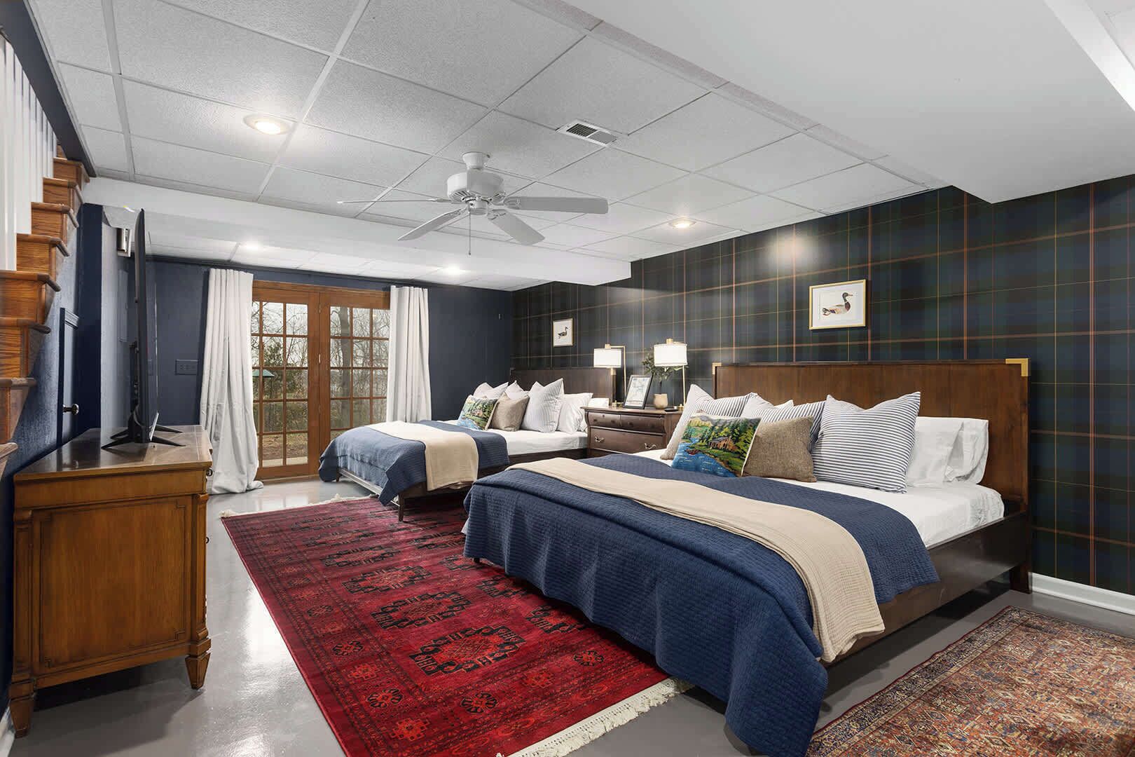 A hotel room with two beds, a wooden dresser, a red rug, and a ceiling fan.