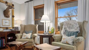 Una habitación acogedora con muebles a cuadros, una cabeza de ciervo en la pared y un ventanal con vistas.