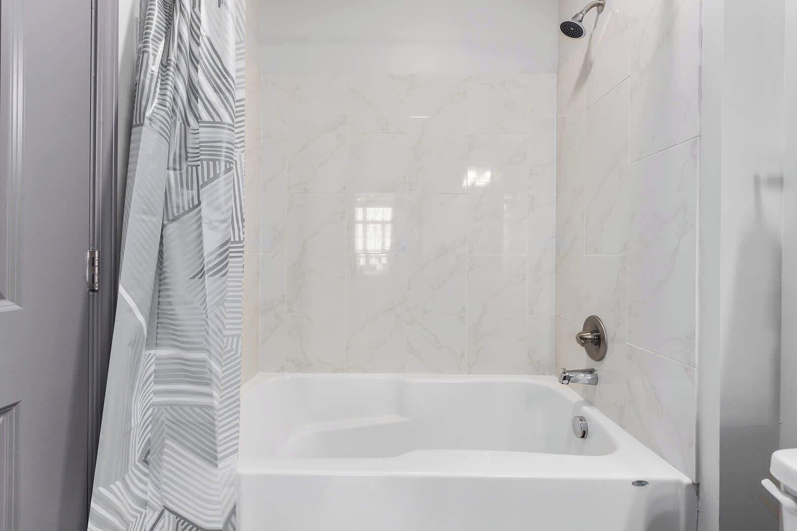 Uma casa de banho moderna com banheira branca, azulejos de mármore e chuveiro com chuveiro de mão.