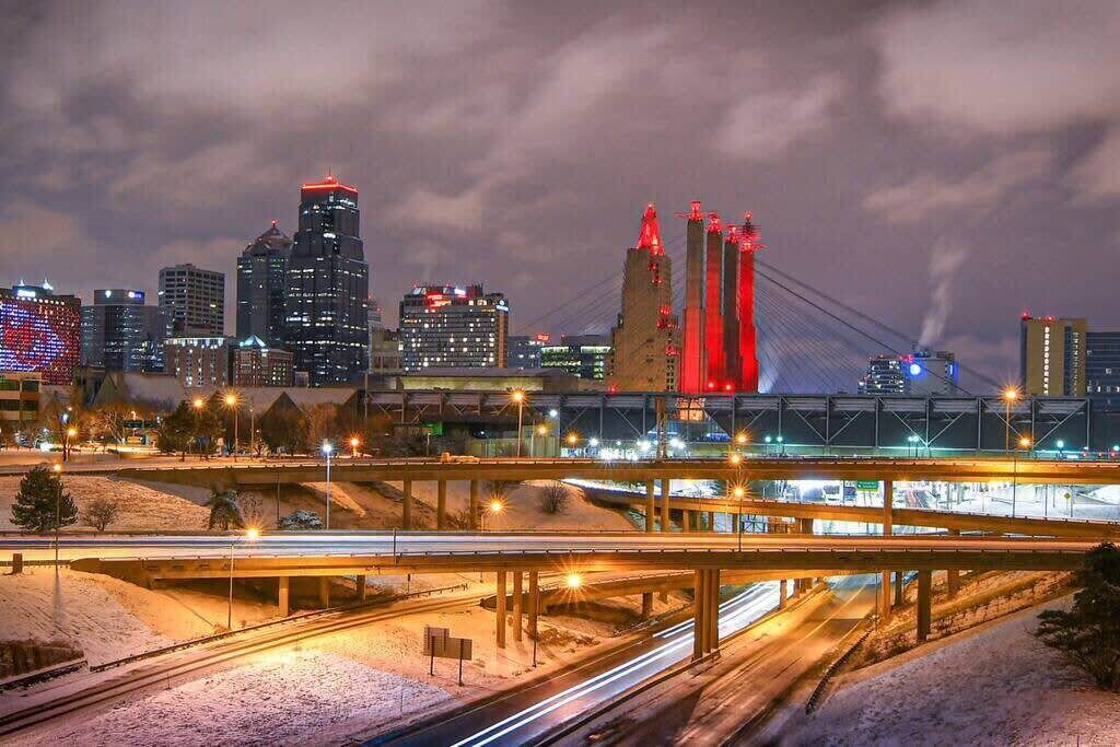 A cityscape at night with illuminated buildings and a prominent bridge with red lights.