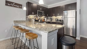 A modern kitchen with dark wood cabinets, stainless steel appliances, and a granite island with bar stools. - 2 King Beds Apartment_Great Amenities_Sleeps 4 (Olathe)