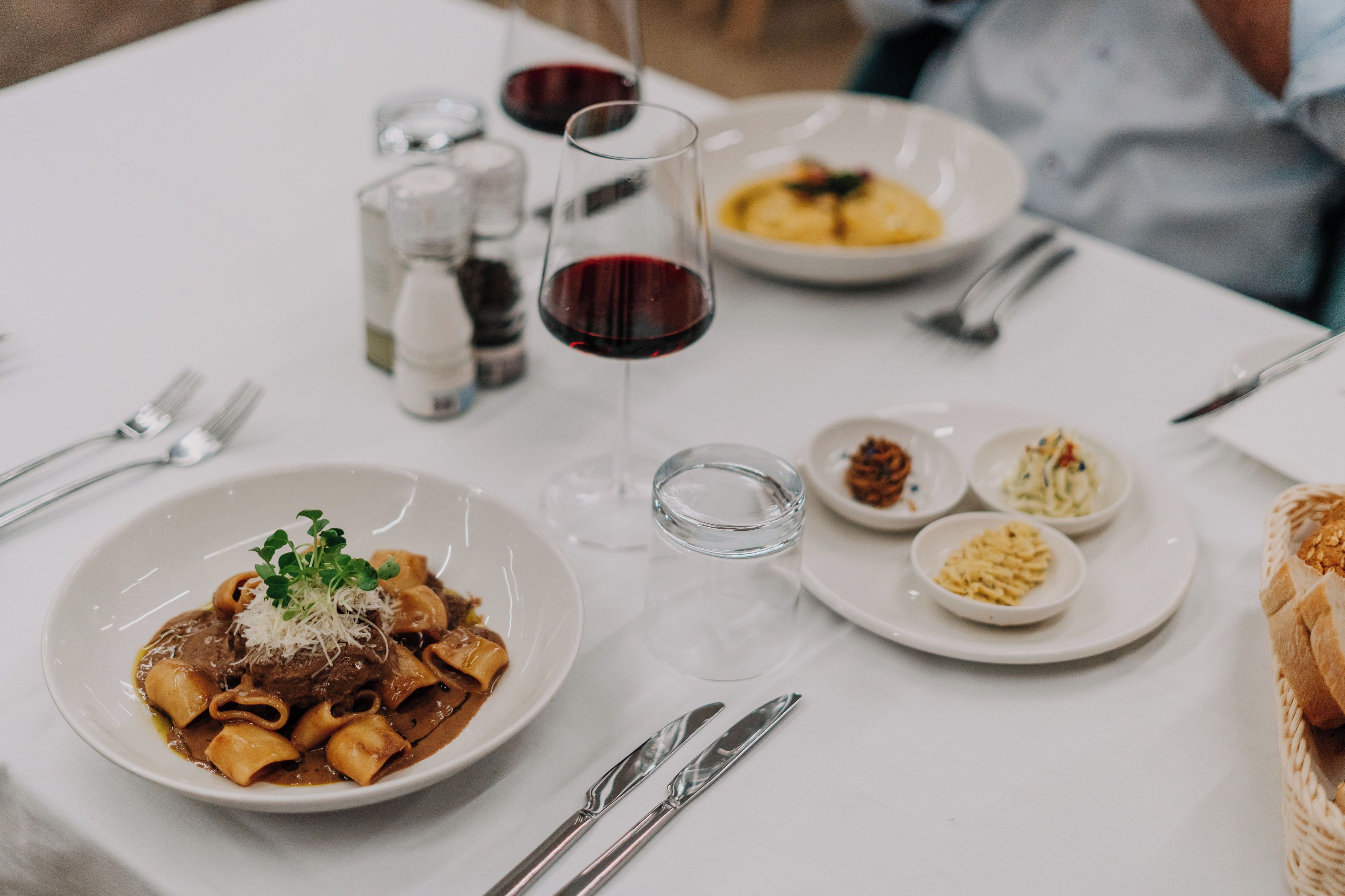 A dining table with plates of food, glasses of red wine, and cutlery.