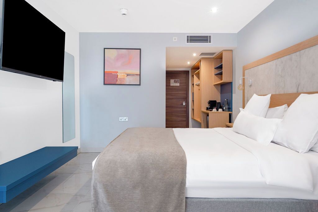 Une chambre d’hôtel moderne dotée d’un grand lit, d’un téléviseur à écran plat, d’un tableau au mur et d’un dressing.