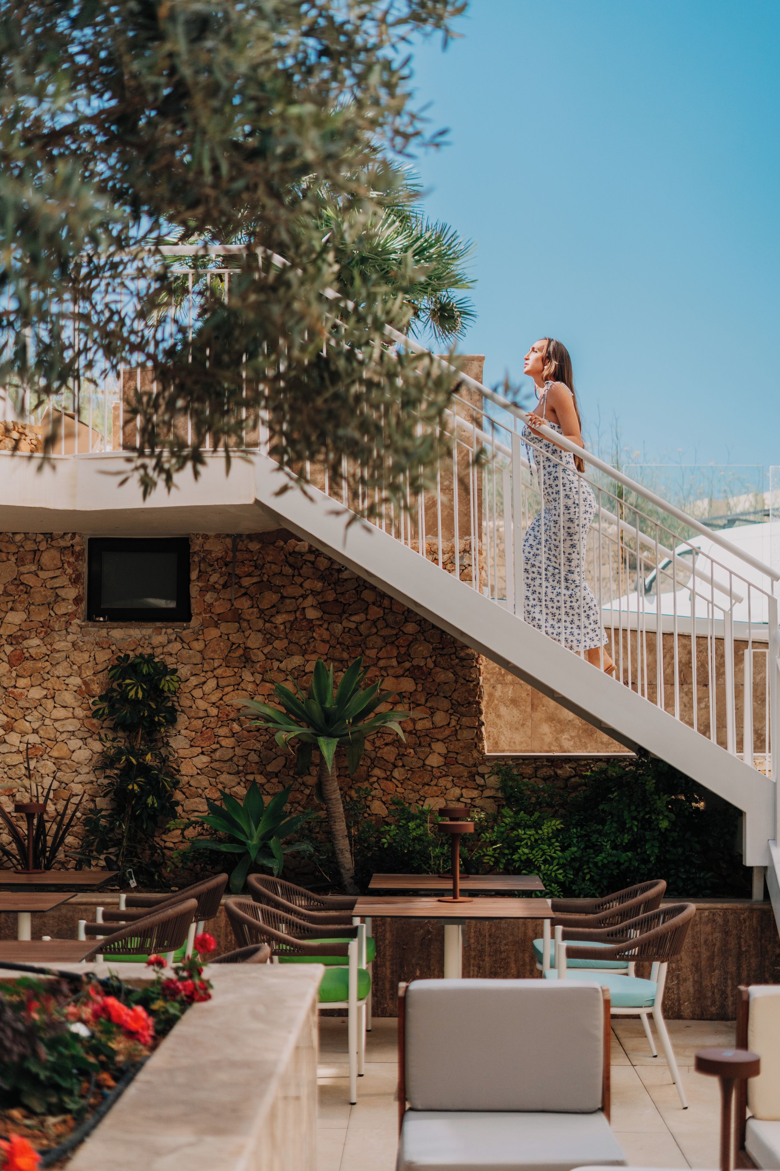 A woman on a staircase with a view of a stone wall and outdoor seating area.