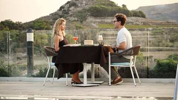 A dining table with chairs, a pool, and a view of a hill with a cross.