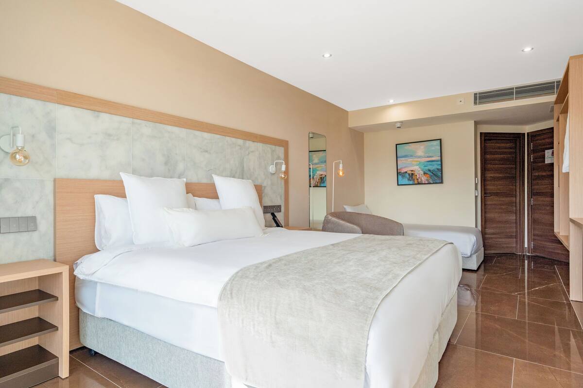 Quarto de hotel com uma cama grande, uma mesa de cabeceira, um espelho e um quadro na parede.