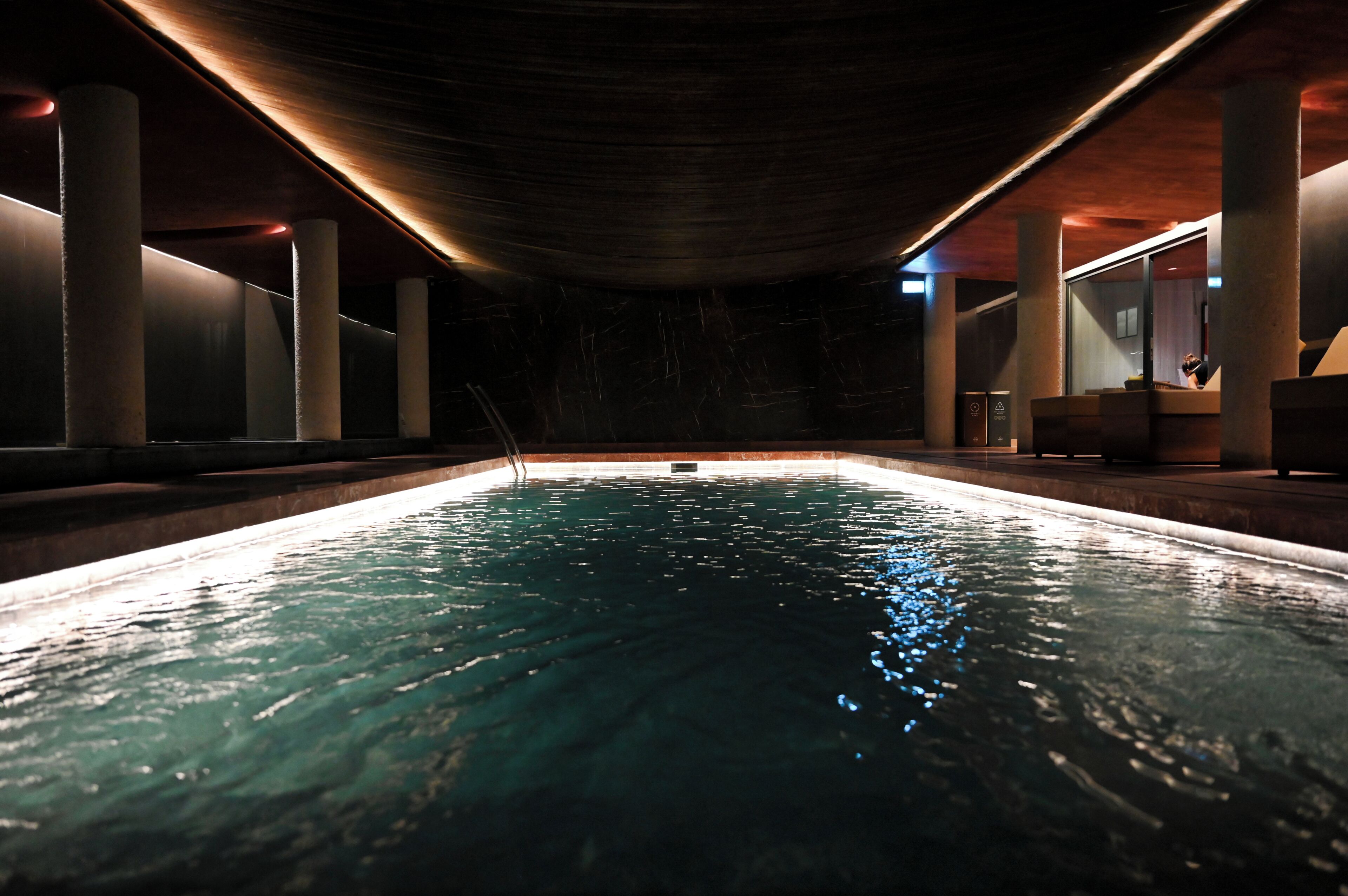 An indoor swimming pool with a dark ceiling and walls, surrounded by pillars.