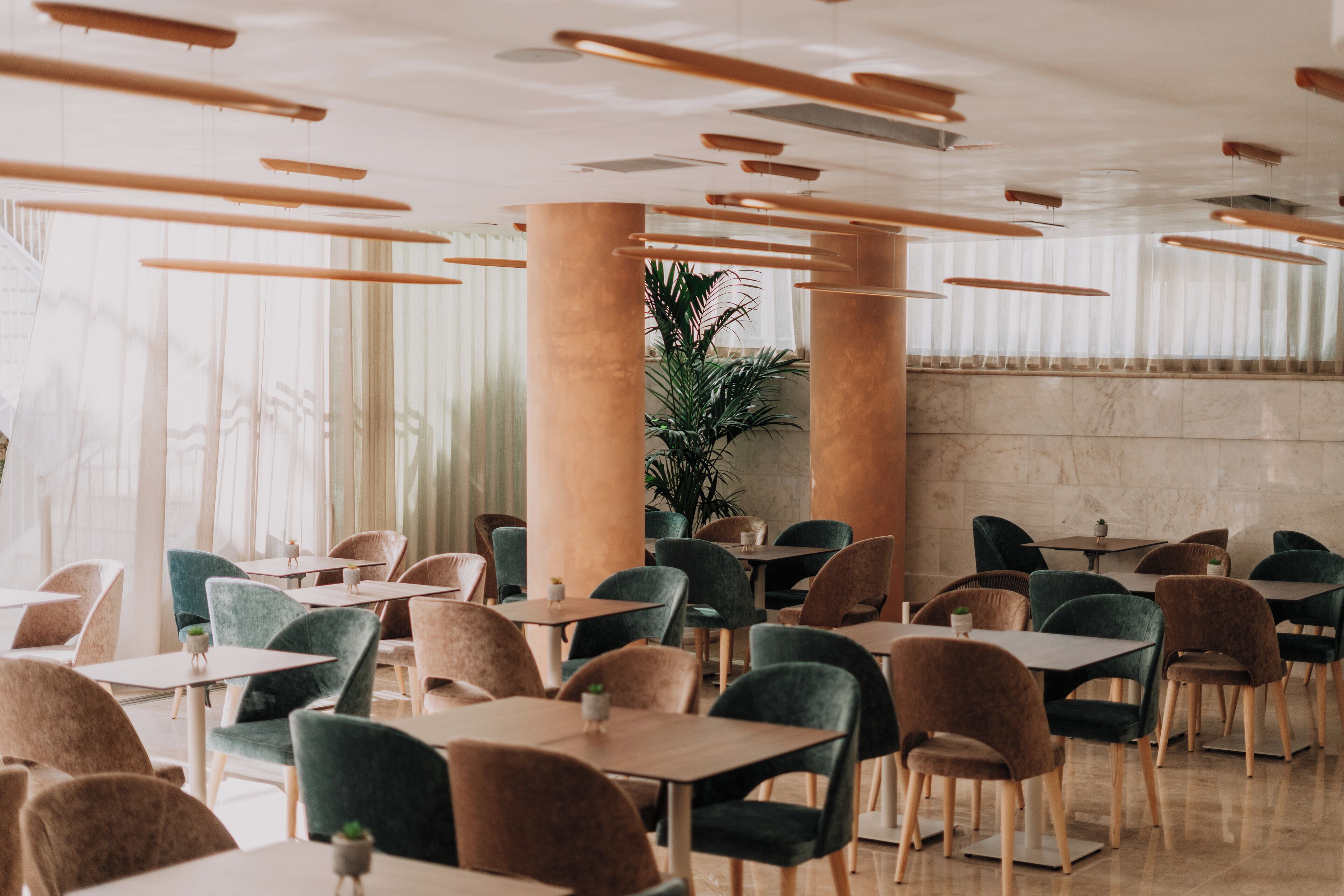 A modern restaurant interior with multiple tables and chairs, large columns, and hanging light fixtures.