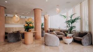 Um lobby moderno com colunas imponentes, assentos confortáveis e um arranjo floral central.