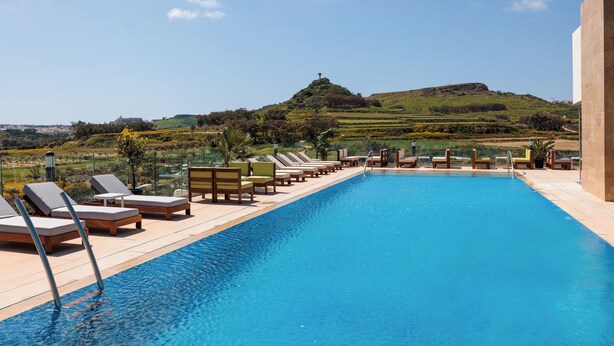 Piscina com espreguiçadeiras e vista para uma colina com uma cruz.