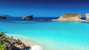 Mar turquesa e transparente com formações rochosas e uma praia de areia.