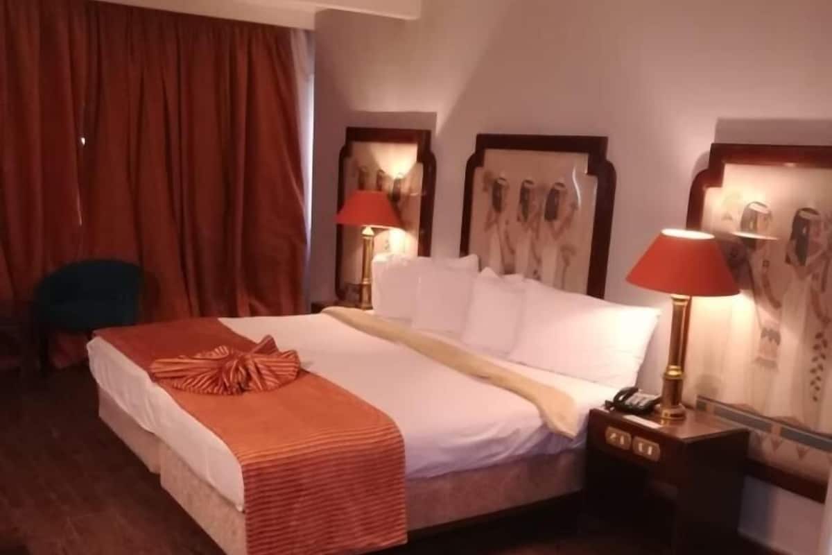 A hotel room with a large bed, two bedside lamps, a nightstand, and a chair.