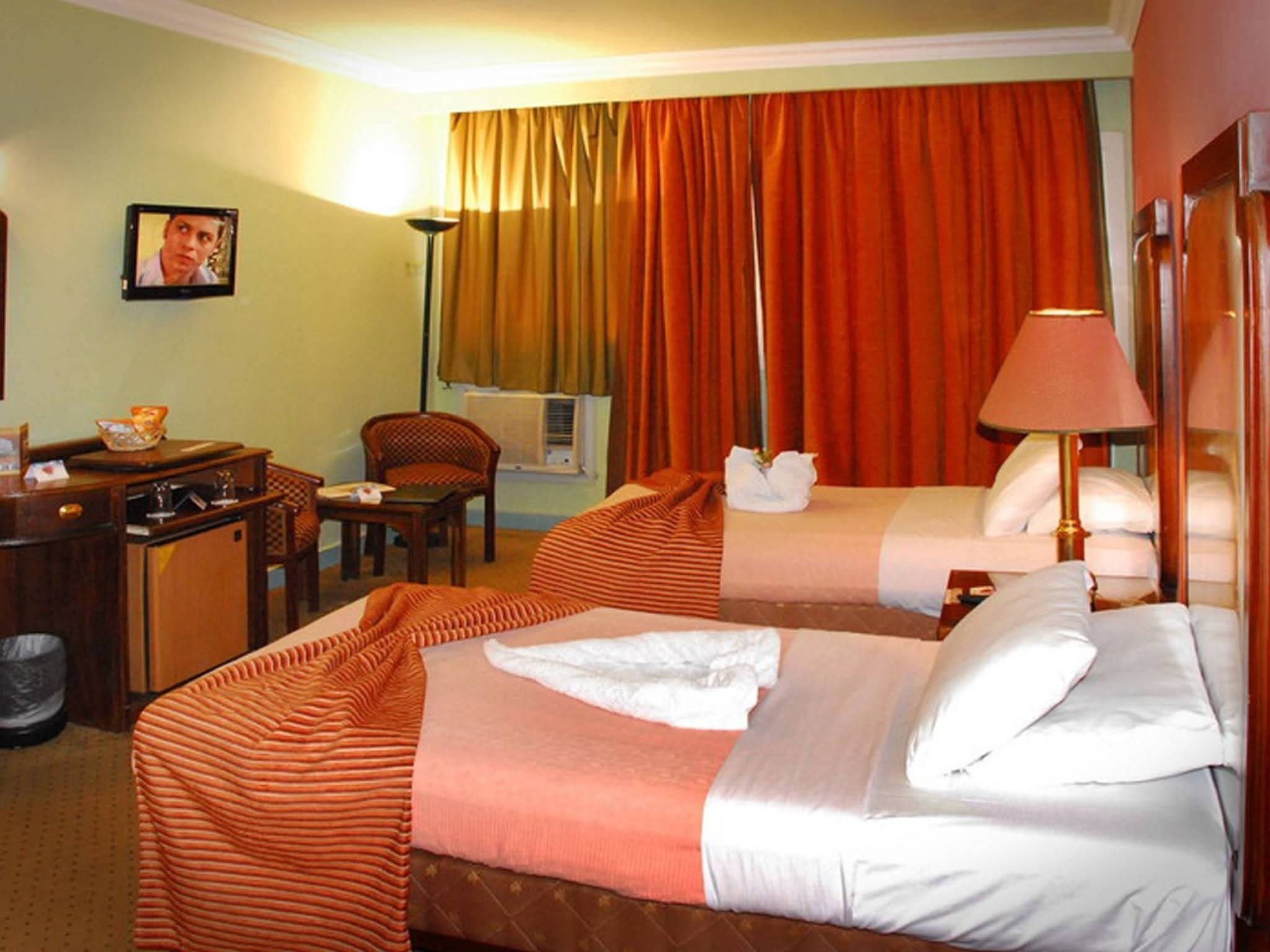 Una habitación de hotel con dos camas, un escritorio, una silla, una lámpara y un cuadro en la pared.