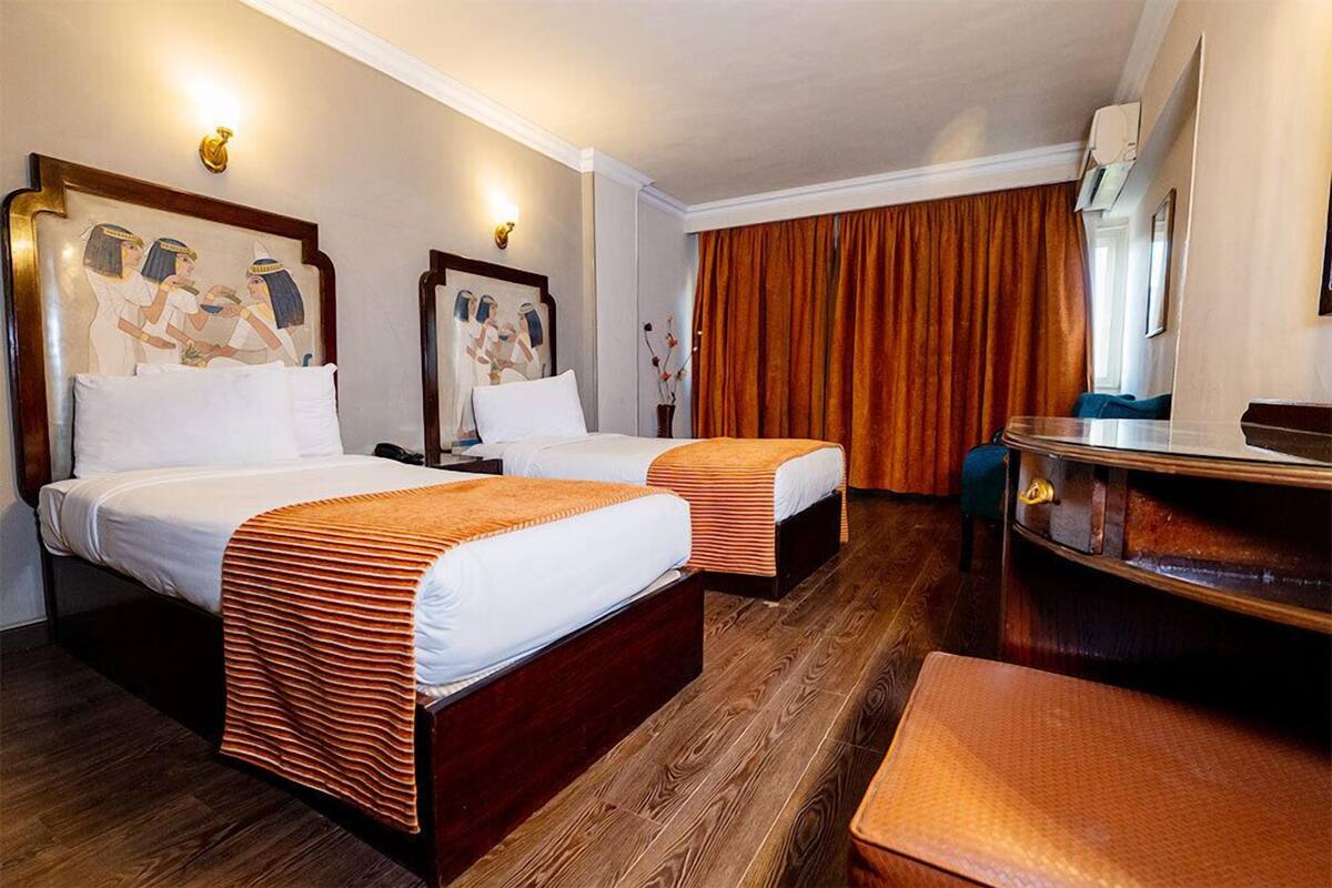 A hotel room with two beds, a wooden floor, a desk, and a large window with curtains.