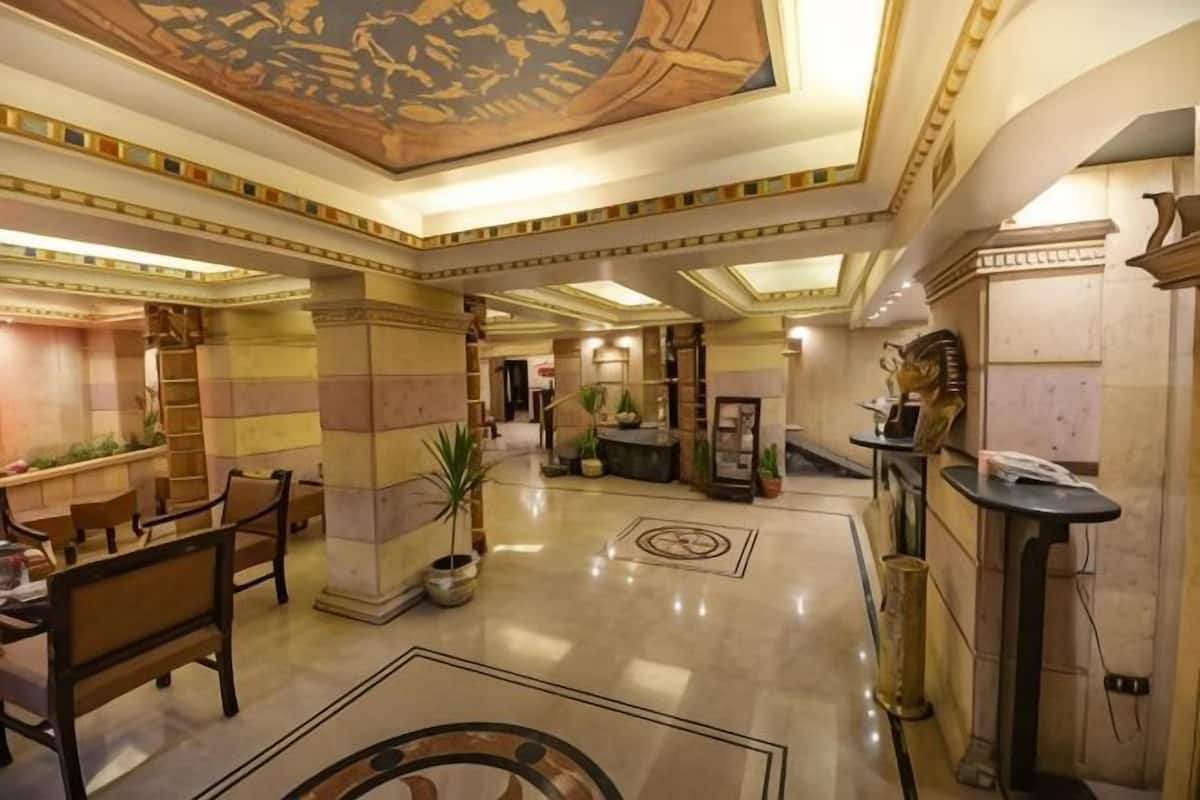 A spacious lobby with a high ceiling, marble flooring, and a central seating area with chairs and tables.