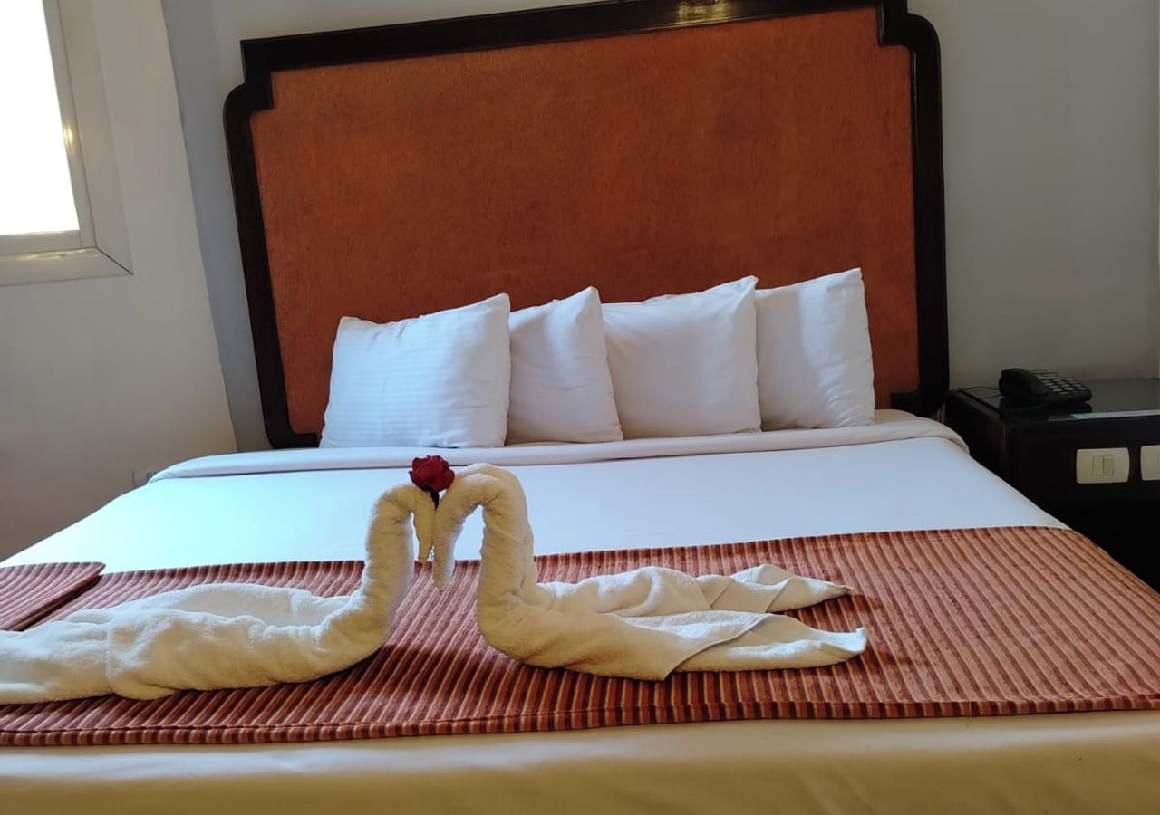 A hotel room with a bed, pillows, a swan-shaped decoration, and a striped rug.