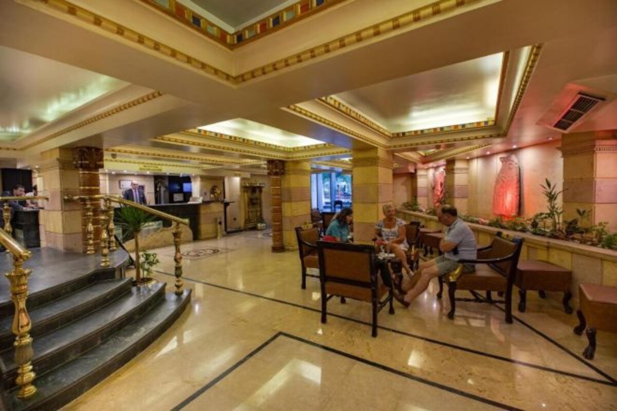 A spacious lobby with marble flooring, a grand staircase, and a seating area with tables and chairs.