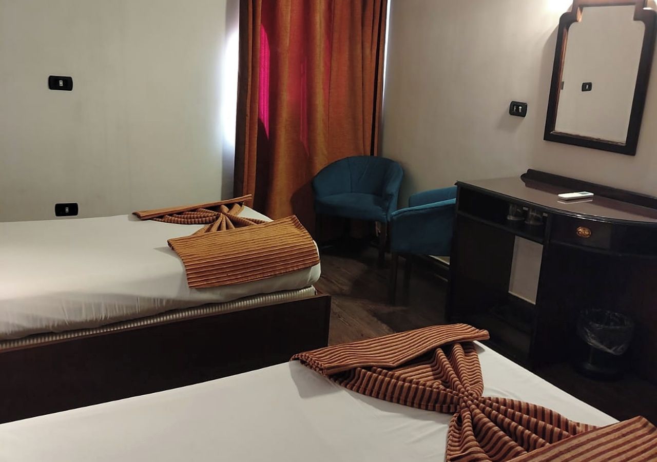A hotel room with two beds, a desk, a chair, and a mirror.