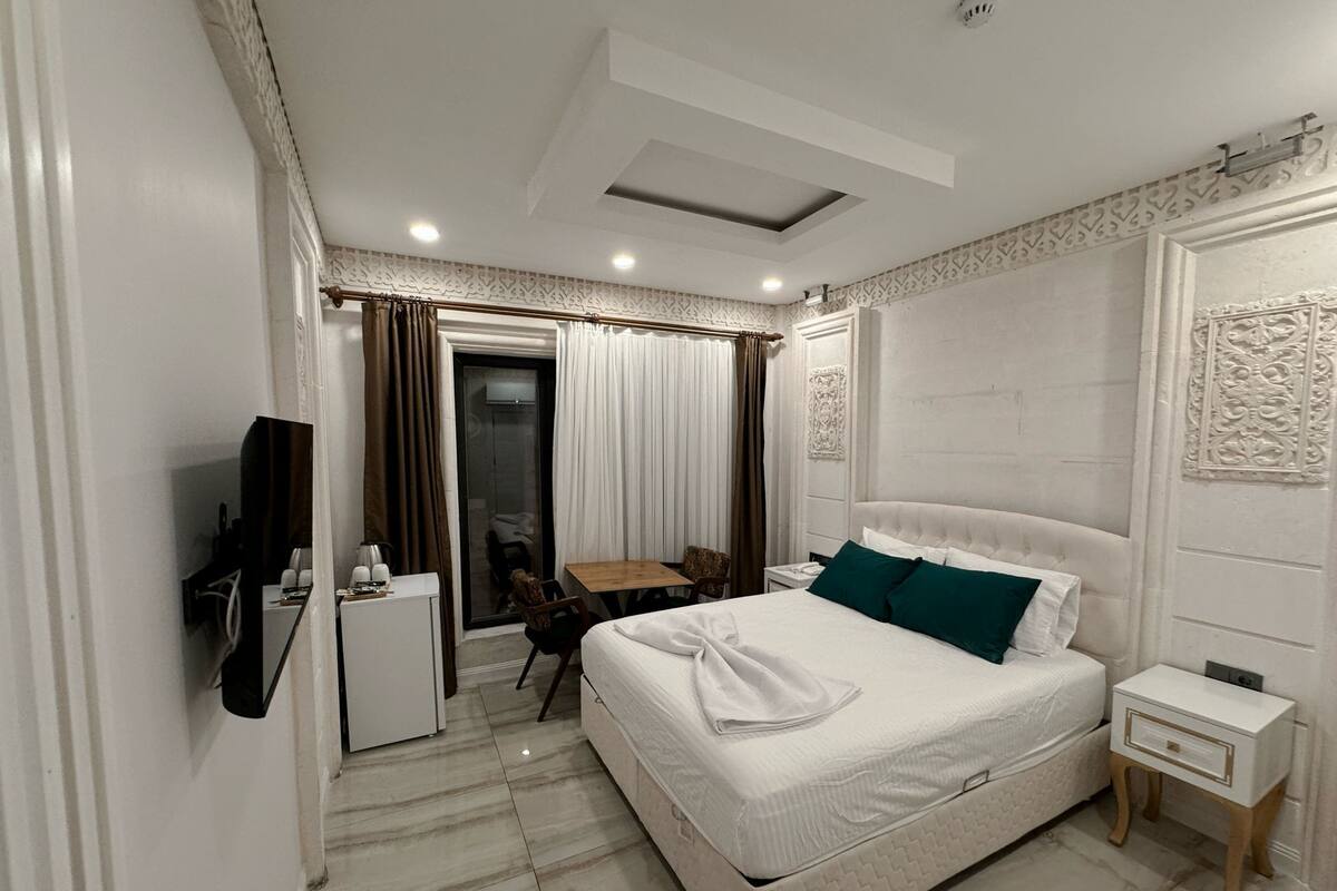 Ein Hotelzimmer mit einem Bett, einem Schreibtisch, einem Stuhl, einem Fernseher und einer Tür, die auf einen Balkon führt.