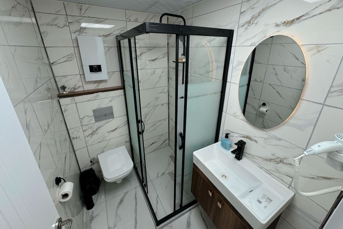 Ein modernes Badezimmer mit einer begehbaren Glasdusche, Marmorfliesenboden, einem weißen Waschbecken mit Spiegel und einem Handtuchhalter.