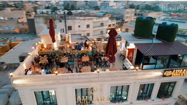 Una terraza en la azotea con mobiliario exterior, un refrigerador de Coca-Cola y un cartel que dice 'AMARA HOTEL & CAFE'.