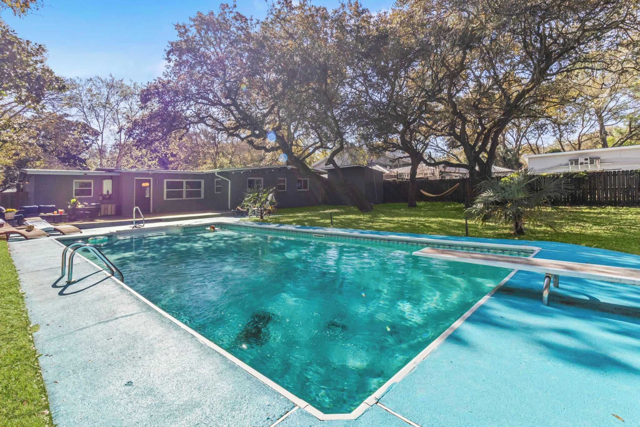 A rectangular swimming pool with a metal ladder on the left side, surrounded by a grassy yard and trees.