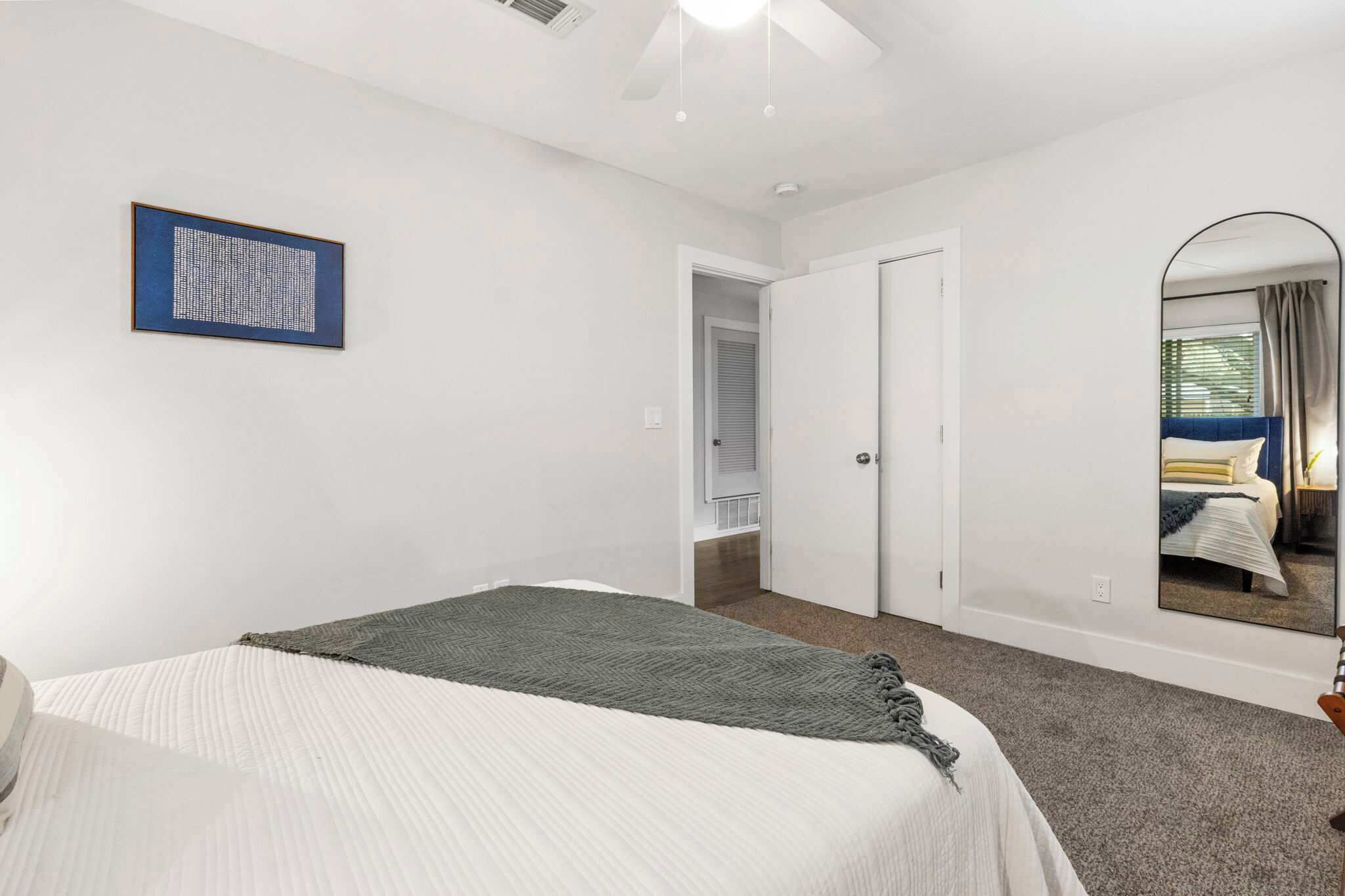 A bedroom with a bed, a framed artwork, a door, and a mirror reflecting a bed.