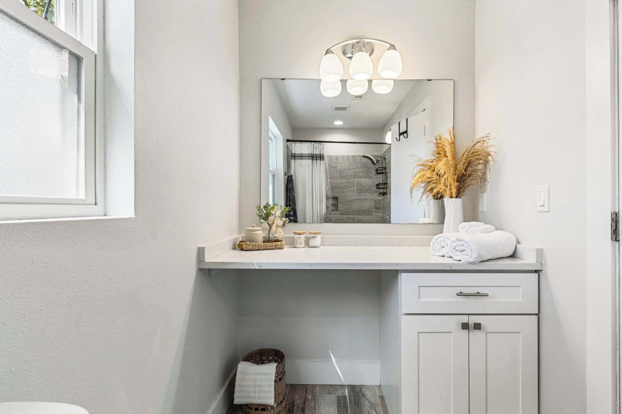 A modern bathroom with a large mirror, white vanity, and a shower area.